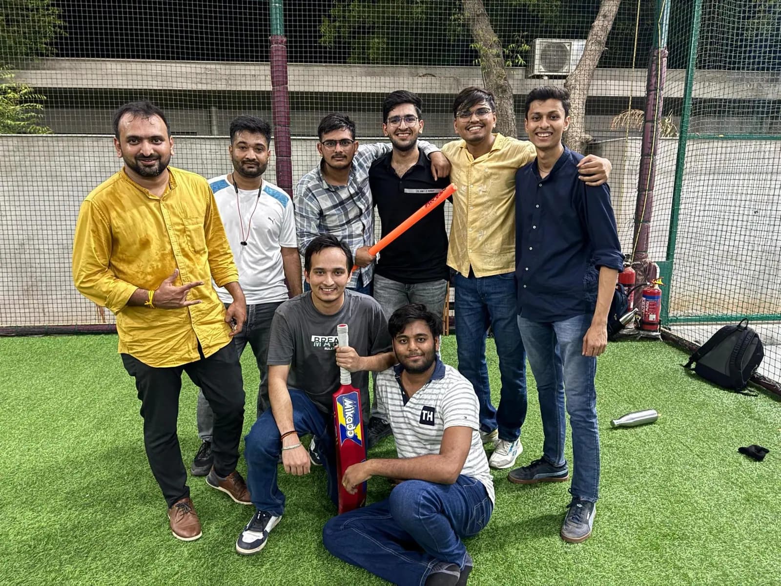The team playing cricket outdoors, one colleague holding the bat
