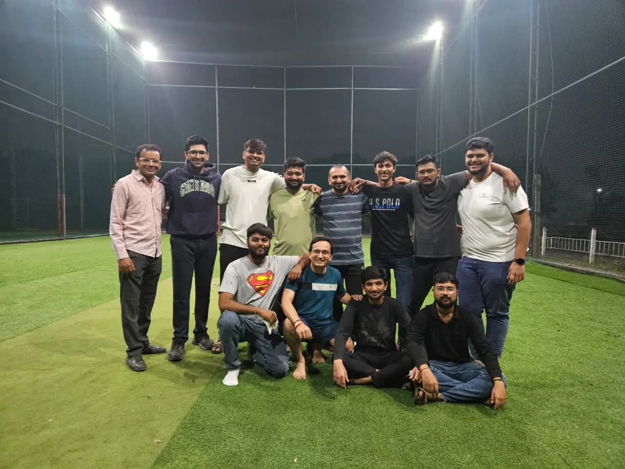 Team photograph on a floodlit box-cricket turf at night