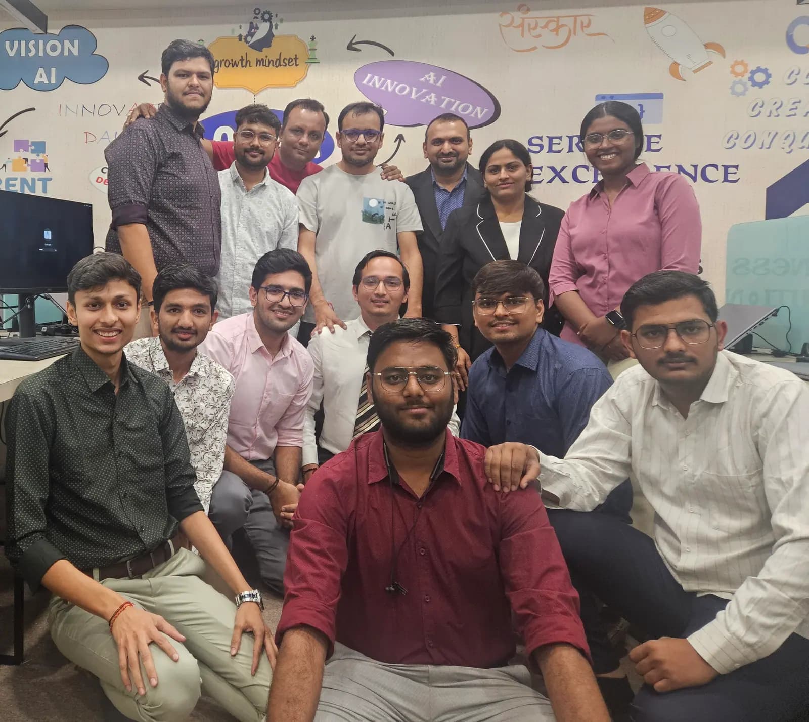 The wider Gothi Tech team assembled in front of the 'Service Excellence' office wall